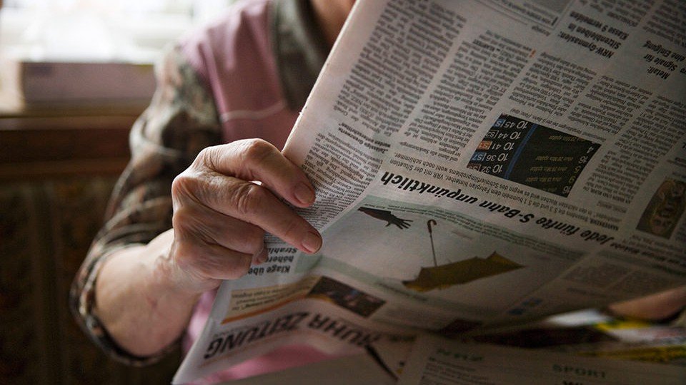 Ältere Frau liest Zeitung verkehrt herum